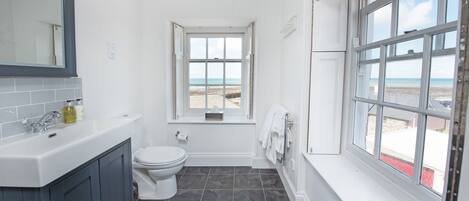 Un baño con lavamanos blanco, gabinetes gris oscuro, inodoro blanco y ventana con vista a la playa.
