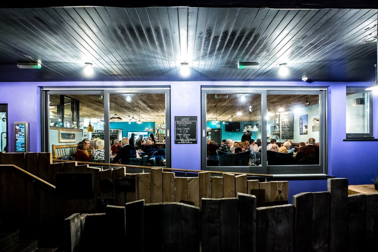 Un restaurant au plafond et aux murs en bois, avec des espaces de restauration séparés par des cloisons en bois, et de grandes fenêtres donnant sur l’intérieur.