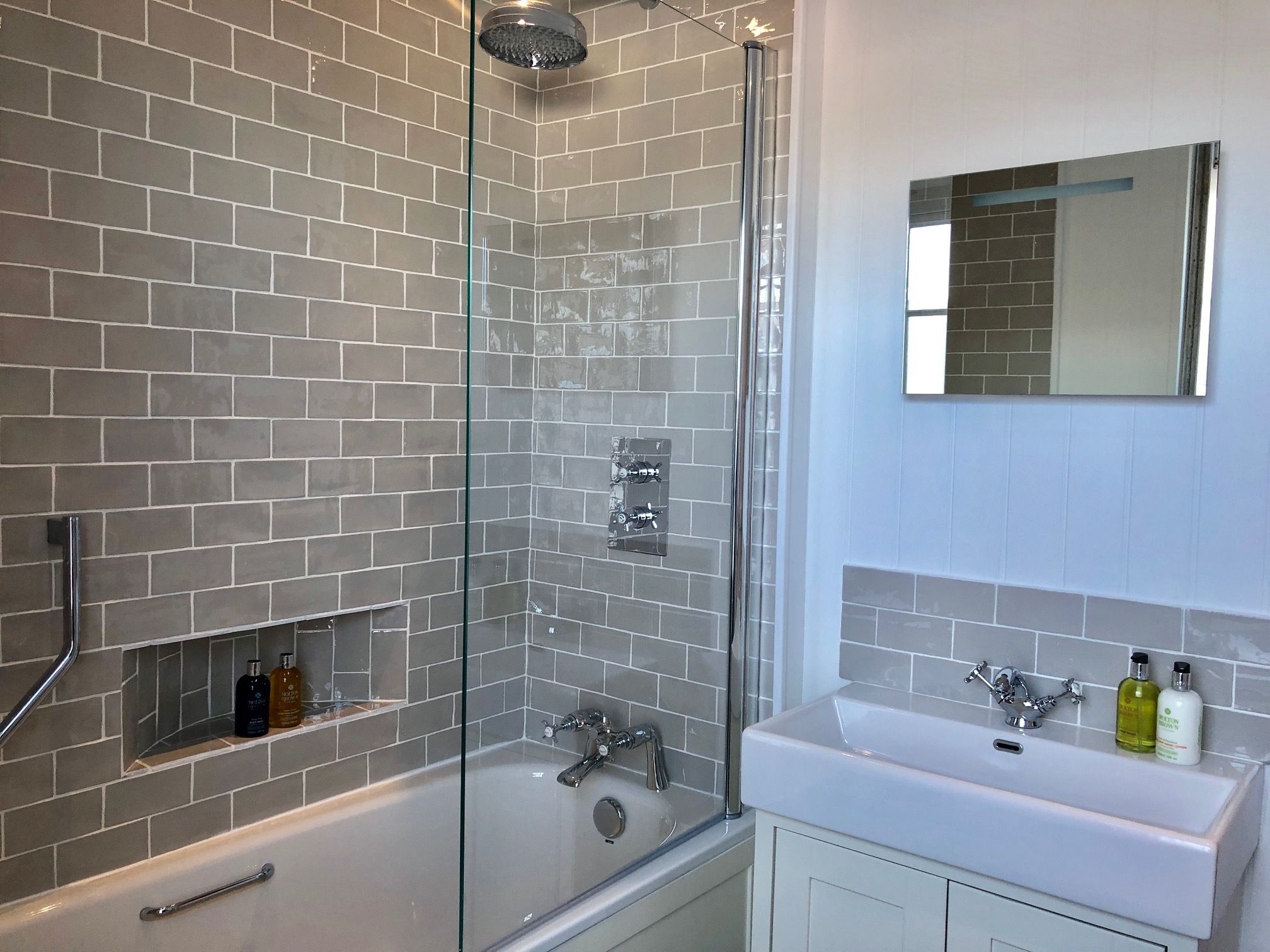 Un baño moderno con cabina de ducha de vidrio, una bañera blanca y un lavabo con artículos de aseo.