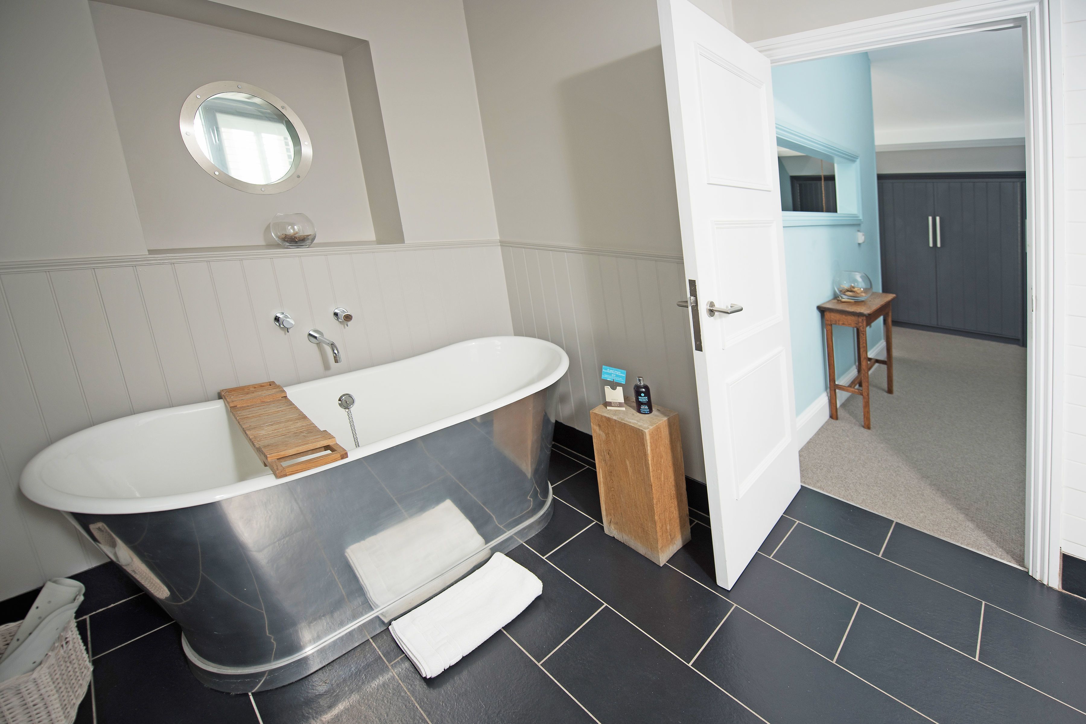 A modern bathroom with a freestanding bathtub, a wooden stool, and a small table with toiletries.