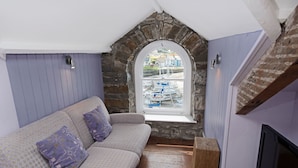 Una habitación acogedora con un arco de piedra en la ventana, un sofá con cojines estampados y un televisor a la derecha.