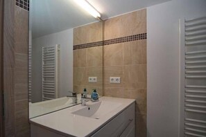 A bathroom with a white sink, a mirror, and beige tiled walls. - Pferdehof Berger (Penig)