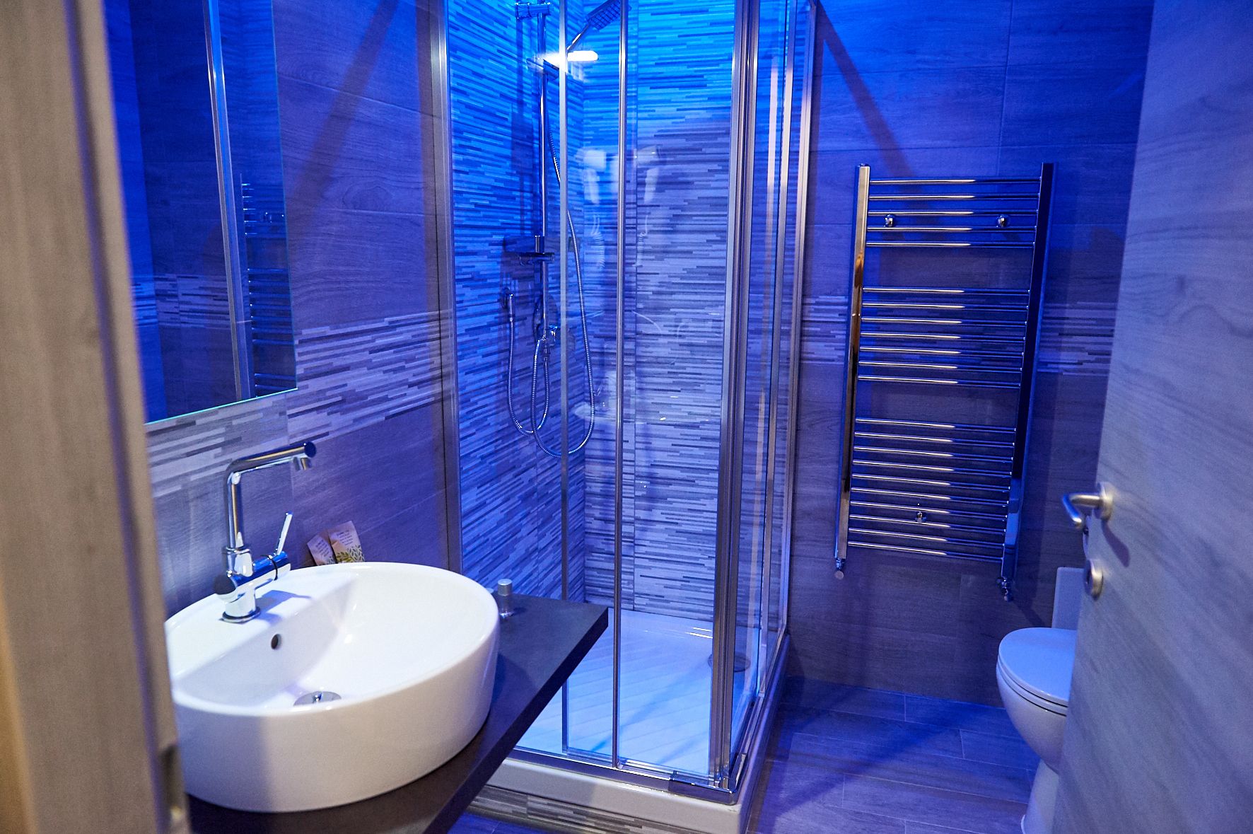 A modern bathroom with a glass-enclosed shower, a white sink, and a towel rack.