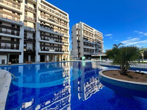Et moderne hotel med flere balkoner, en swimmingpool og en klar blå himmel.