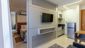 A modern hotel room with a large bed, a TV mounted on a wall, a kitchenette, and a wooden door. - Venice Park Hplus Long Stay (Guará)