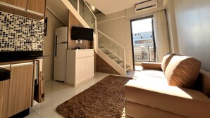 A modern living room with a sofa, a flat-screen TV, a refrigerator, and a staircase leading to an upper floor. - Venice Park Hplus Long Stay (Guará)