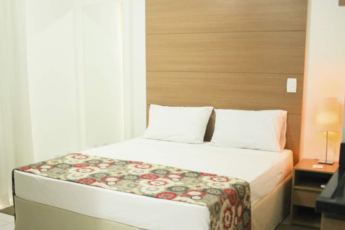 Une chambre d’hôtel avec un lit, une table de chevet, une lampe et un rideau.