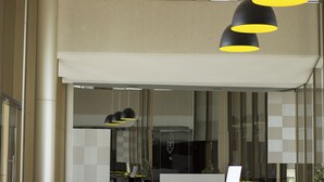 A modern interior with a large window, a reception desk, and a black pendant light. - Venice Park Hplus Long Stay (Guará)