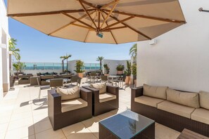 An outdoor patio with wicker furniture, a glass table, and a large umbrella. - Biarritz Hplus Long Stay (Brasília)