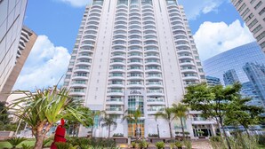 A tall hotel with a central entrance, surrounded by palm trees and other greenery. - Biarritz Hplus Long Stay (Brasília)