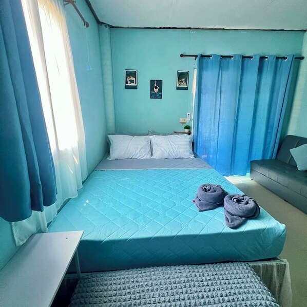 A bedroom with a bed, a small table, a sofa, and a wall with pictures.