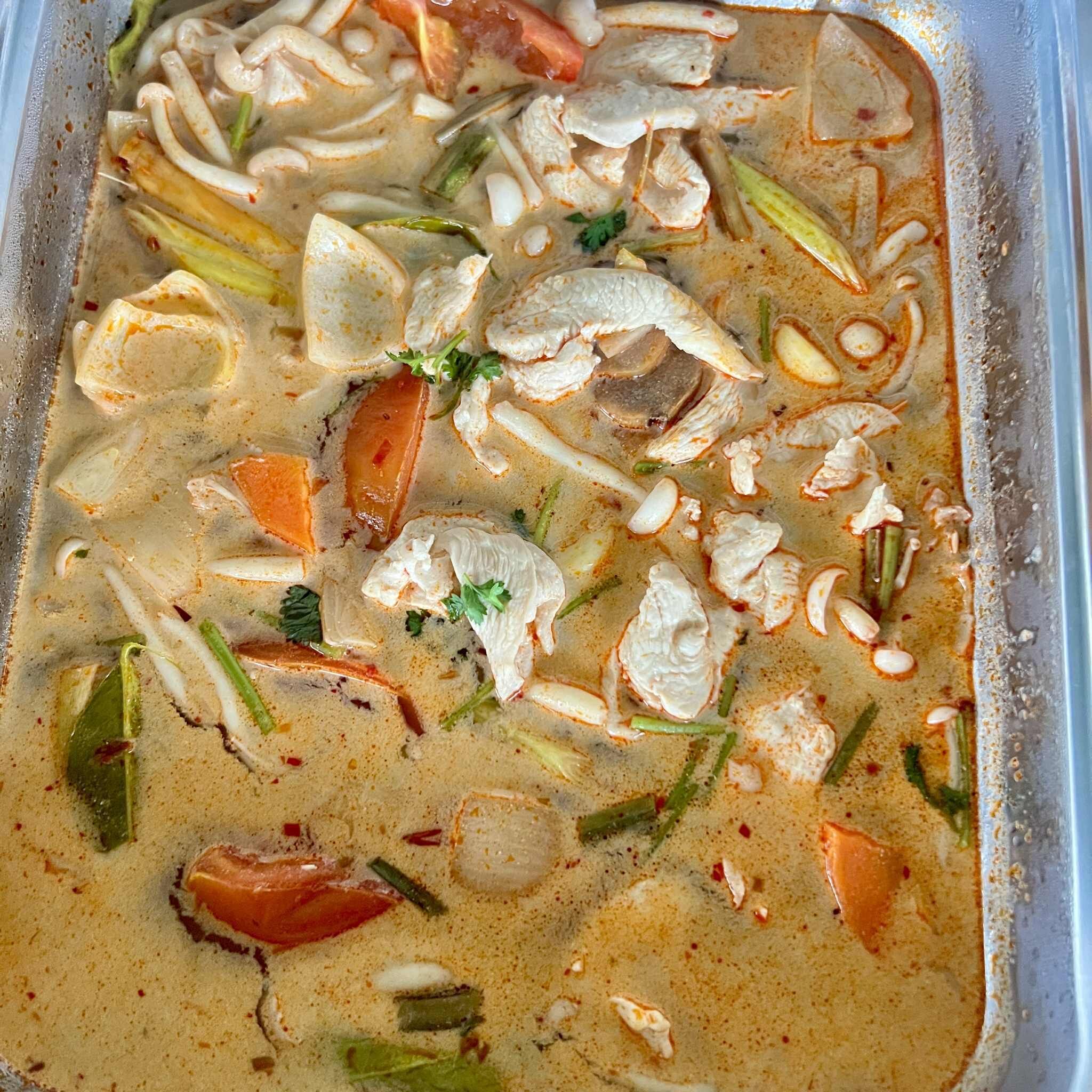 A container of soup with various ingredients like vegetables and herbs.