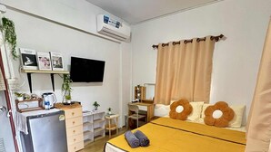 A compact hotel room with a bed, a desk, a small refrigerator, a television, and a window with curtains. - Lee Red House (Ko Kood)