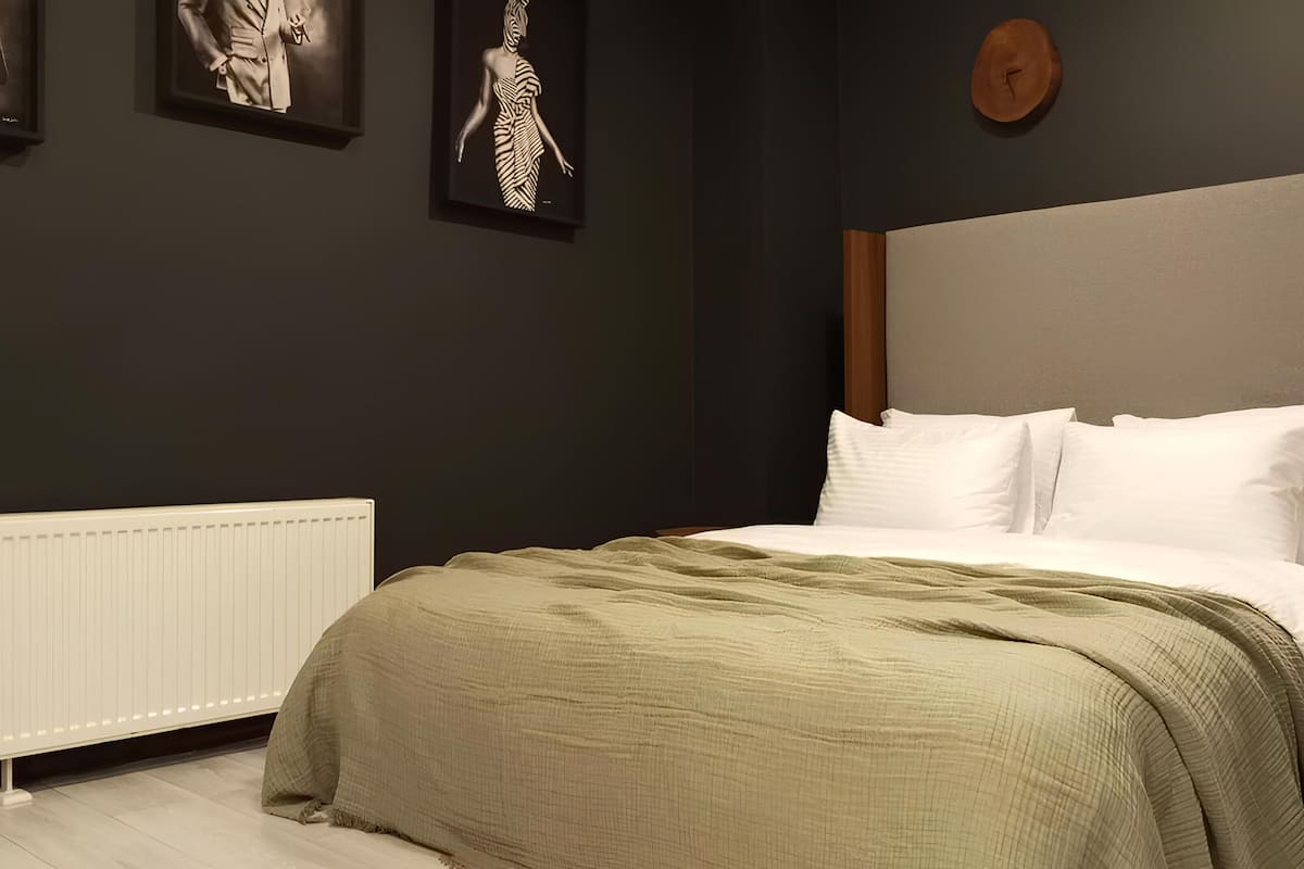 A bedroom with a bed, white pillows, a green blanket, a wooden headboard, and a white radiator.