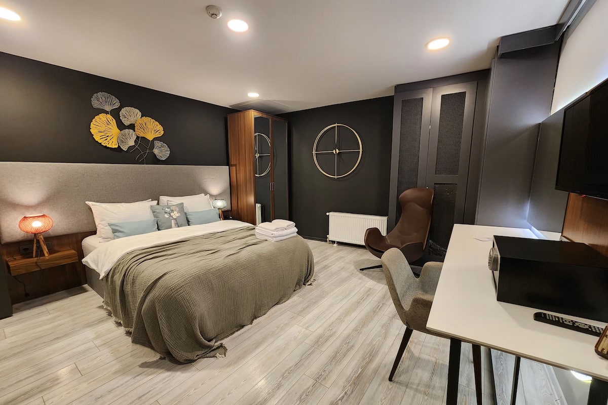 A modern hotel room with a bed, a desk, a chair, a TV, and a decorative wall piece.