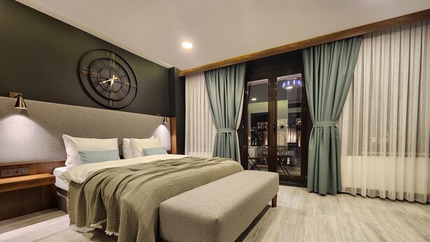 Un dormitorio moderno con una cama grande, un banco, un reloj de pared y vistas a un balcón a través de cortinas traslúcidas.