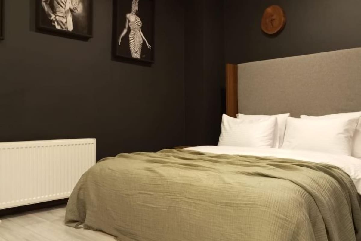 Un dormitorio con una cama, un radiador y dos cuadros enmarcados en la pared.