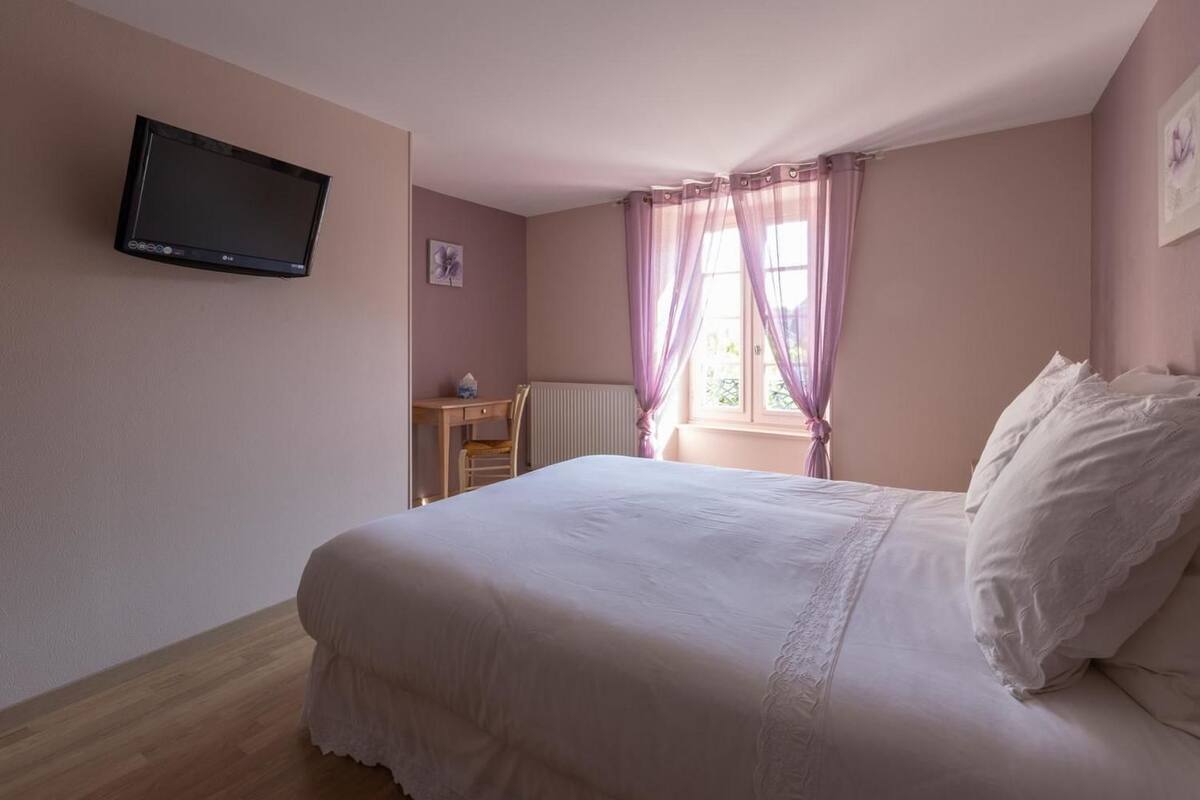 Een slaapkamer met een bed, bureau, stoel, televisie en een raam met gordijnen.
