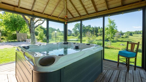 Een hottub in een overdekte buitenruimte met een houten terras en een stoel.