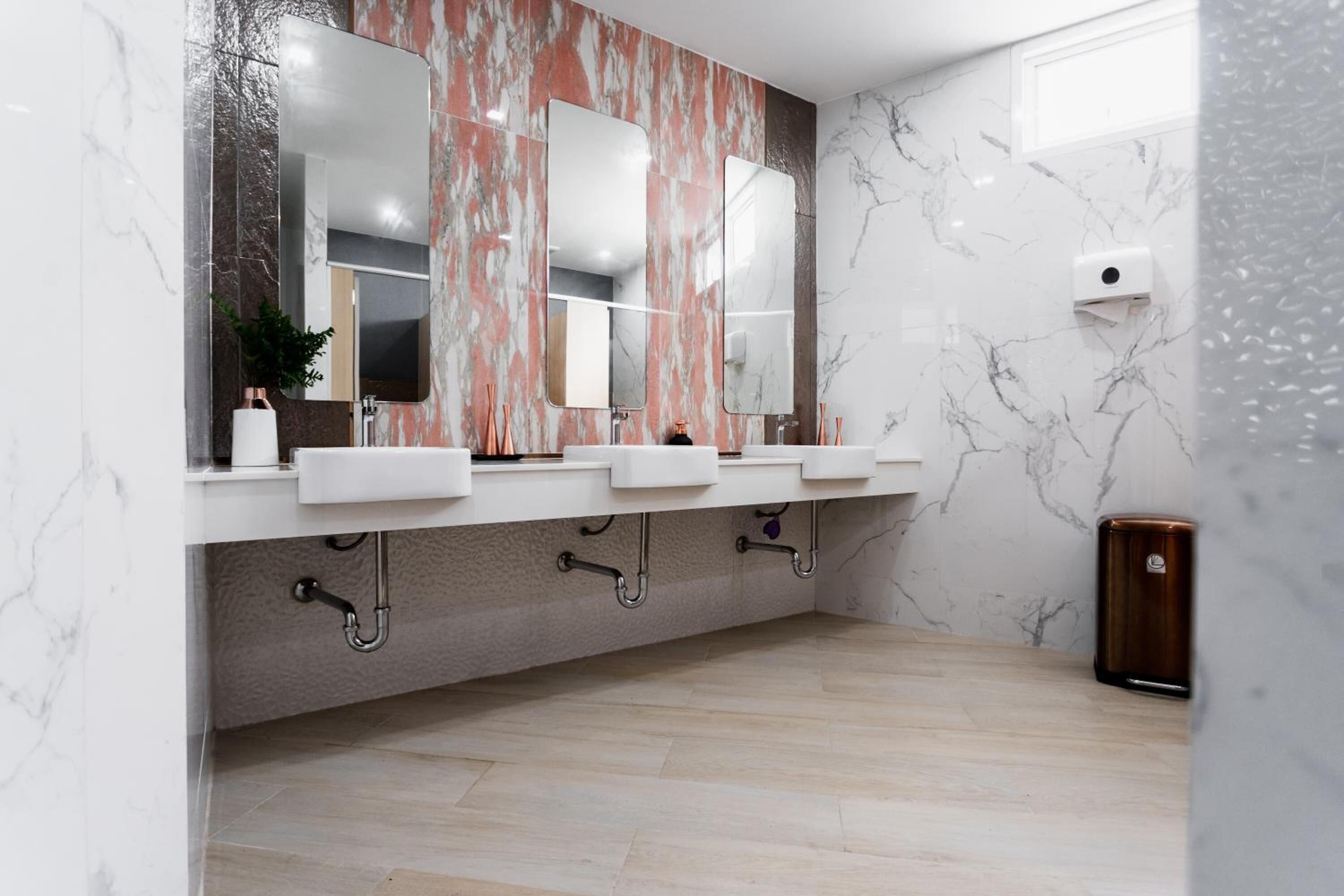 Un baño moderno con tres lavamanos, paredes de mármol y suelo de madera.