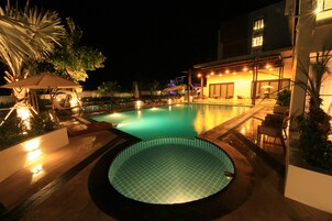 Un área de piscina con jacuzzi, sillas de descanso y una zona de estar cubierta por la noche.