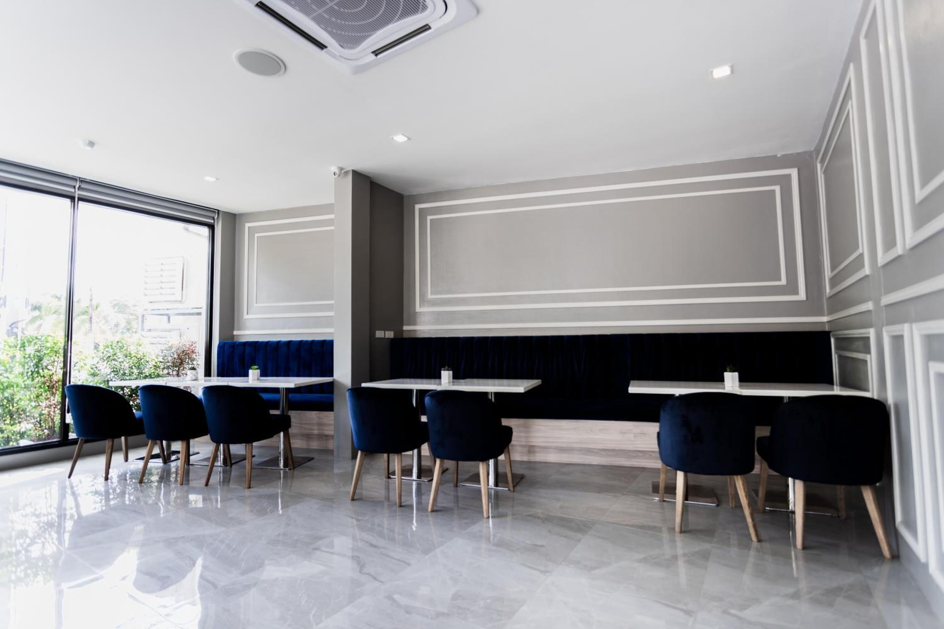 Un restaurant moderne au décor épuré et minimaliste, avec un long comptoir agrémenté de tables et de chaises, de grandes fenêtres offrant une vue sur l’extérieur et un ventilateur de plafond.