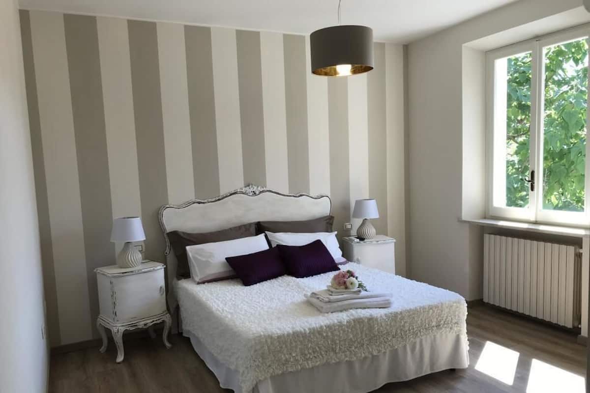 A bedroom with a bed, two bedside tables, a window, and a radiator.