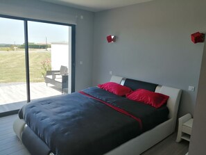 A modern bedroom with a large bed, a sliding glass door to a balcony, and a view of a grassy area. - Le Temps d'un Reve (Eauze)