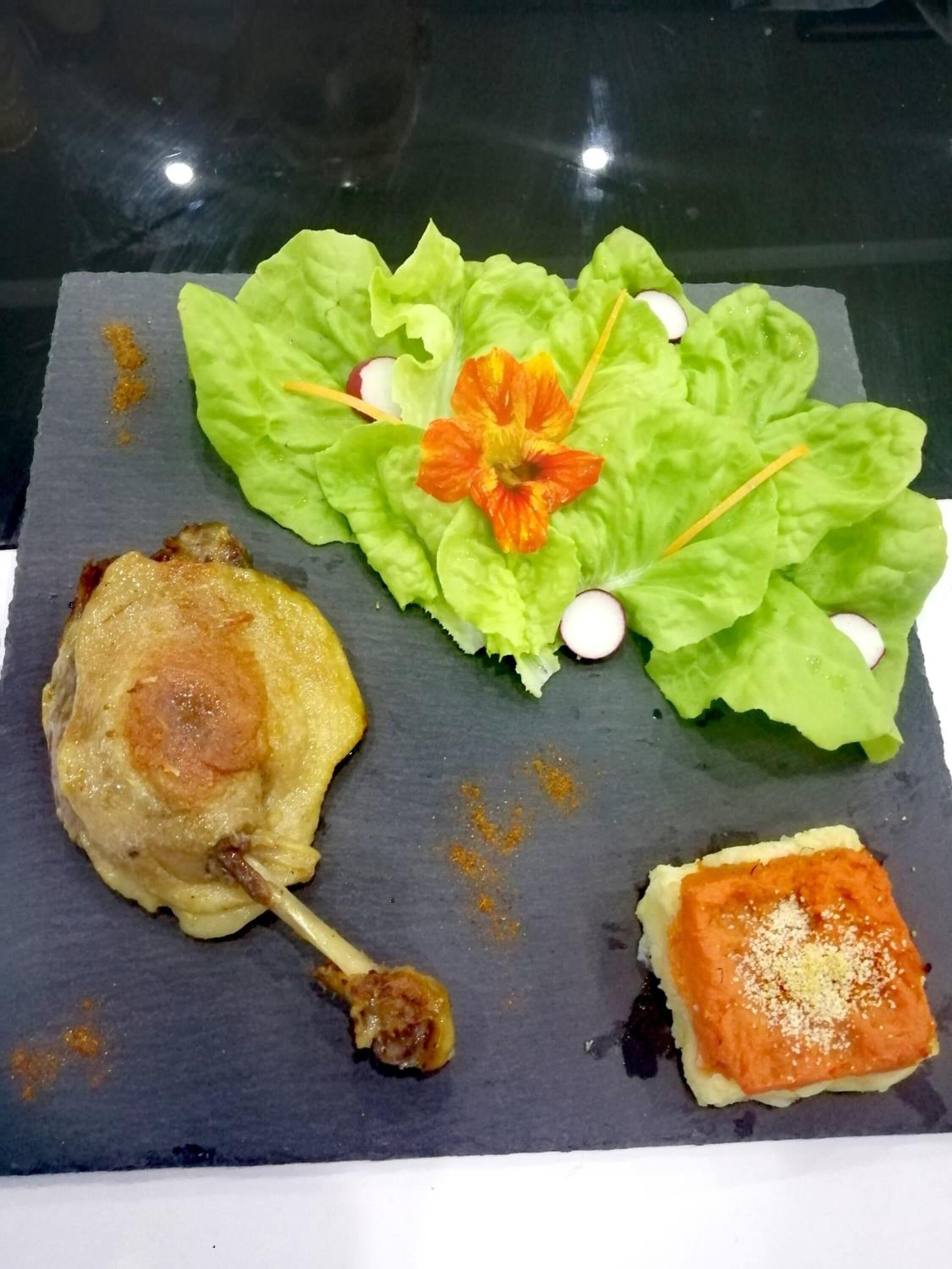 Un plato con un muslo de pollo a la parrilla, un trozo de salmón y un cuadrado pequeño de pan con cobertura.