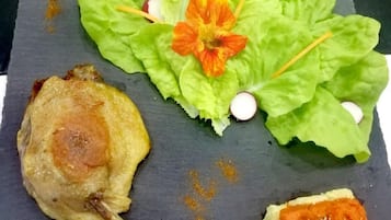 Een bord met een gegrilde kippenpoot, een stuk zalm en een klein broodje met beleg.