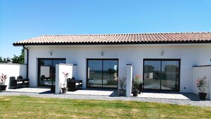 A modern house with a tiled roof, large sliding glass doors, and a patio area with outdoor furniture and potted plants. - Le Temps d'un Reve (Eauze)