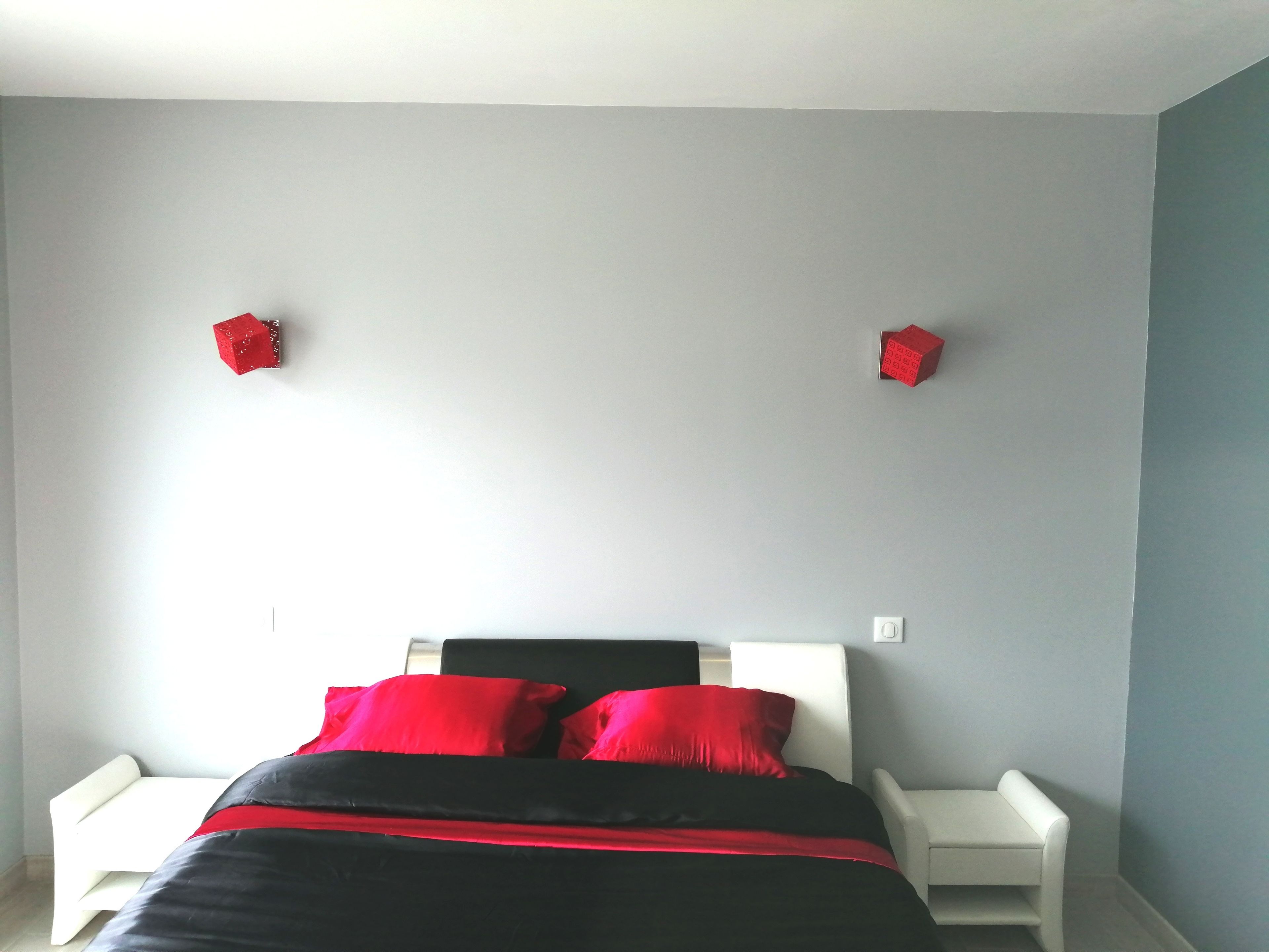 A bedroom with a bed, two nightstands, and two red decorative cubes on the wall.