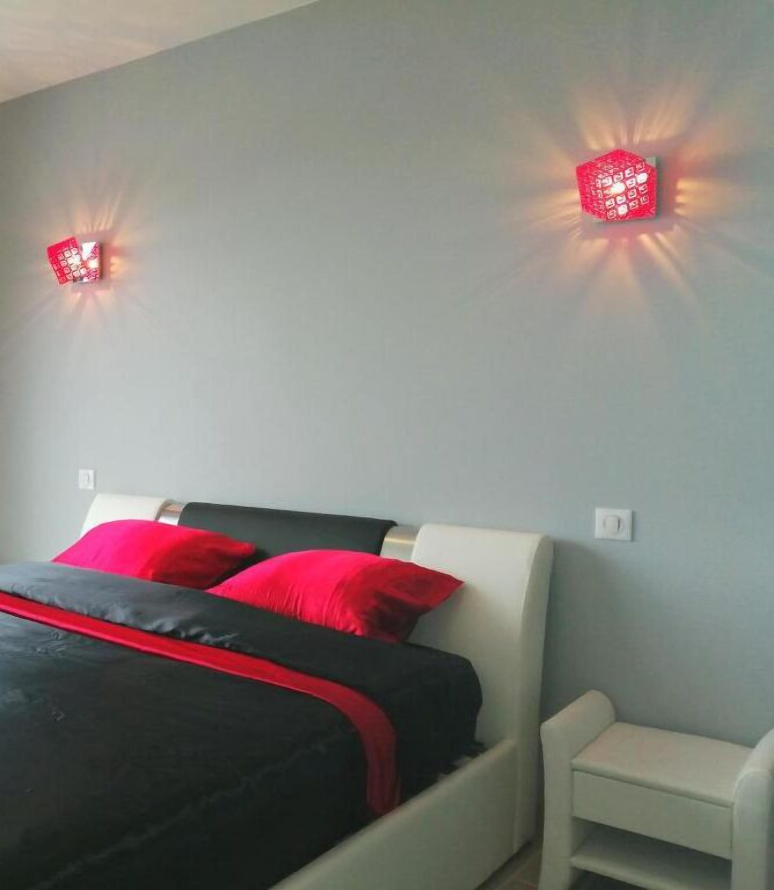 Una cama con ropa de cama negra y roja, un cabecero blanco y dos apliques de pared rojos.