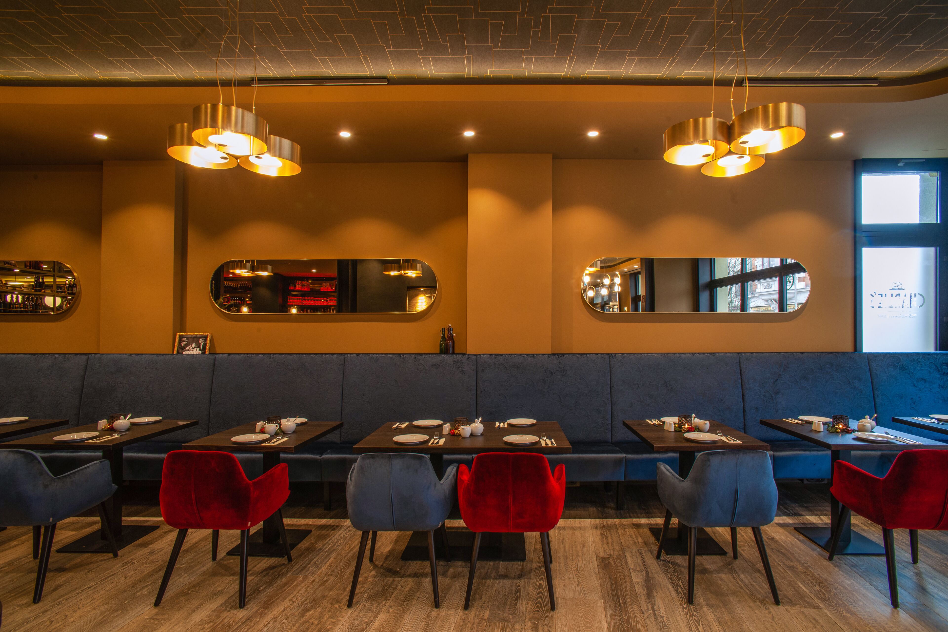 Interior de restaurante con cabinas, mesas redondas y sillas rojas.