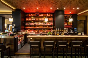 Een bar met meerdere flessenkasten, een bargedeelte en verschillende barkrukken.