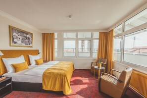A hotel room with a large bed, a desk, a chair, and a window with curtains.