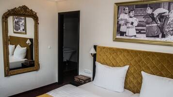 Une chambre d’hôtel avec un grand lit, un miroir, un tableau encadré au mur et une petite table avec une lampe.
