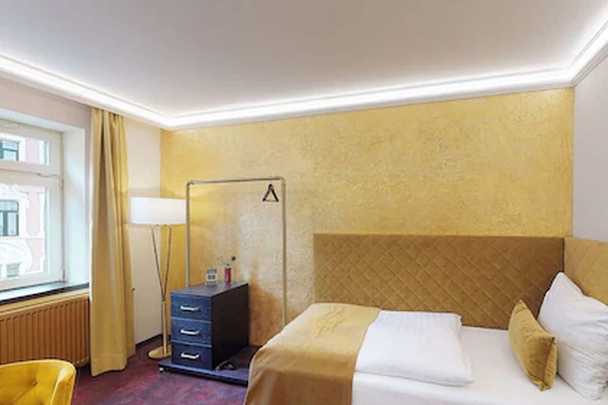 Une chambre d’hôtel avec un lit, une lampe de chevet, une commode et une fenêtre avec des rideaux.