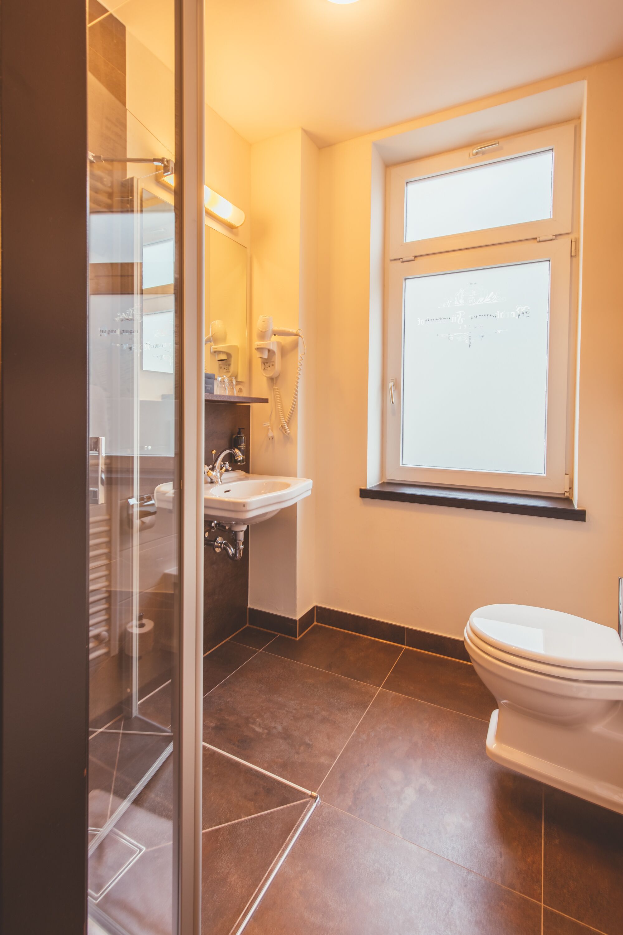 A bathroom with a glass shower enclosure, a sink, a toilet, and a window above the toilet.