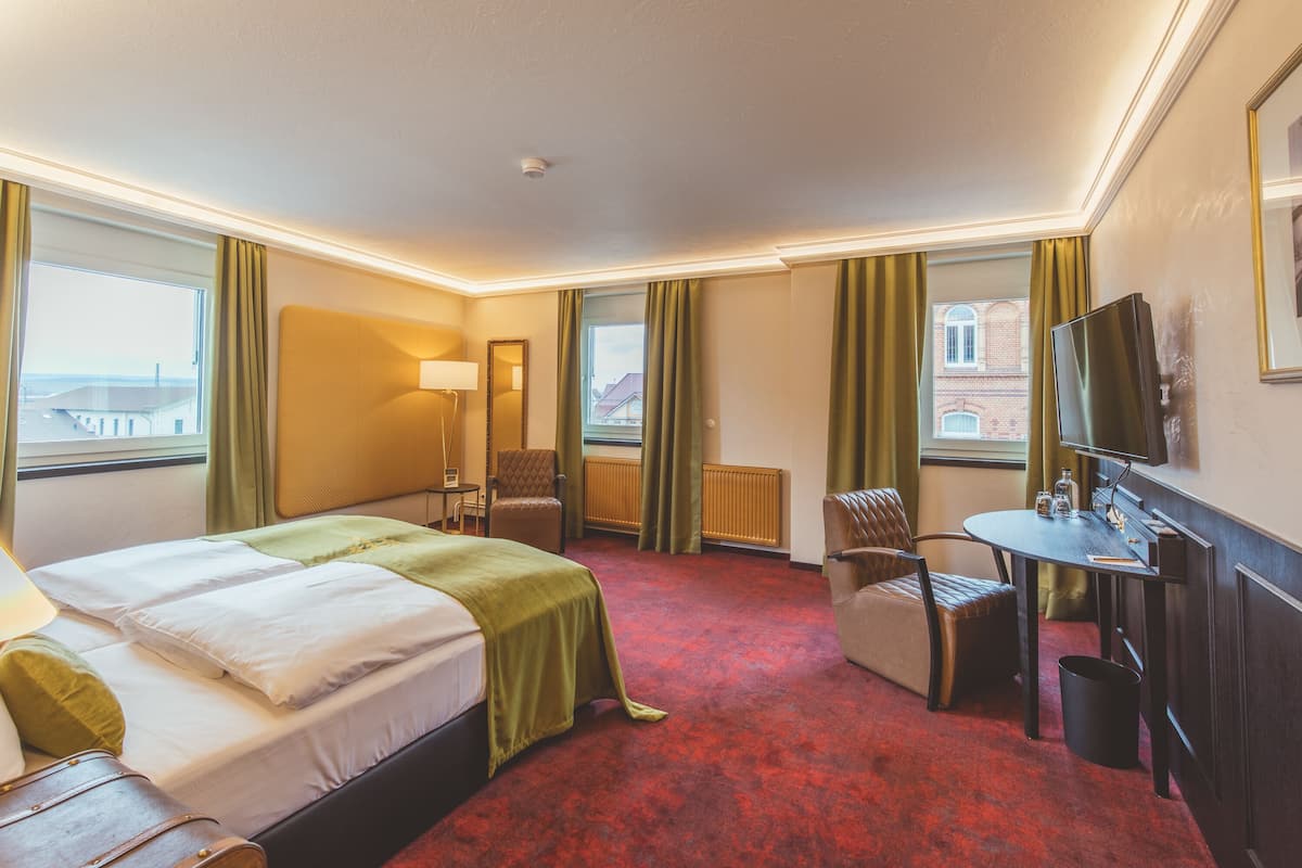 Une chambre d’hôtel avec un lit, un bureau, une chaise, une télévision et une vue sur la ville.