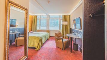 A hotel room with a bed, a desk, a chair, a TV, and a large mirror.