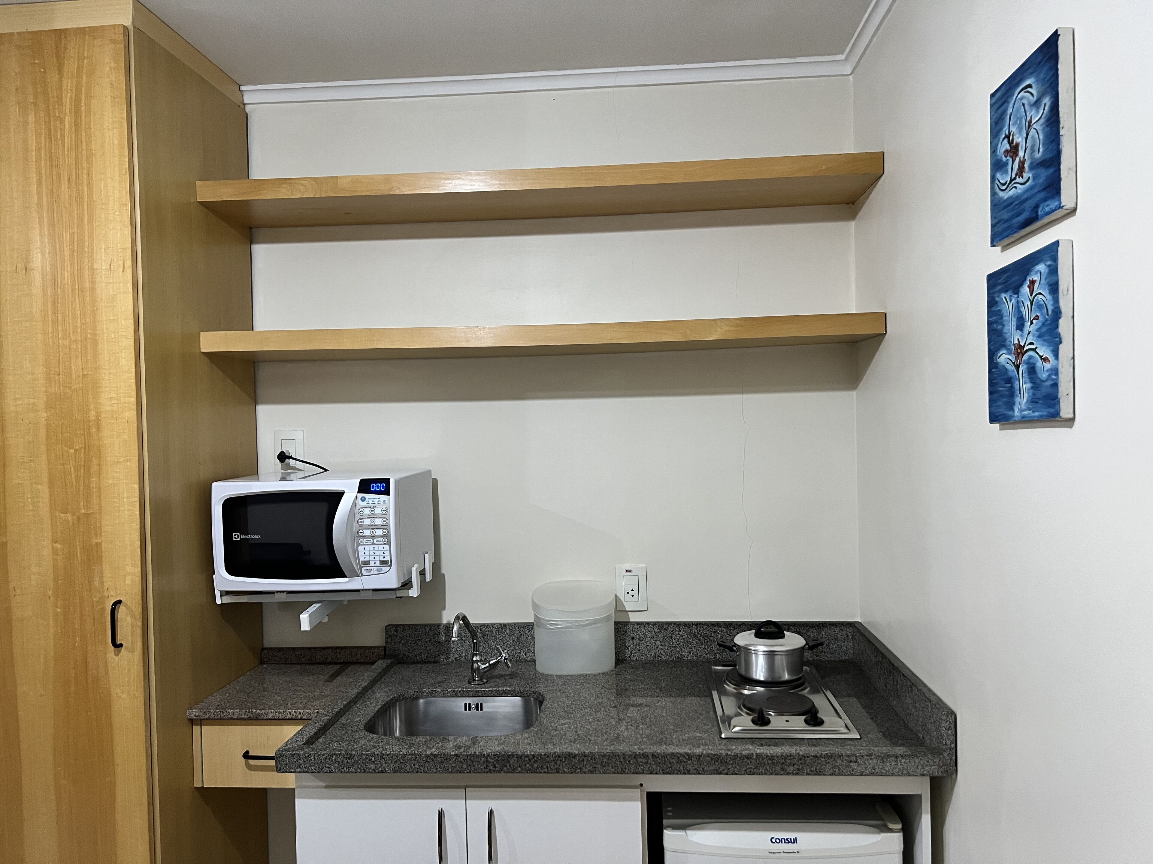 A compact kitchen with a microwave, sink, stove, and wooden shelves.