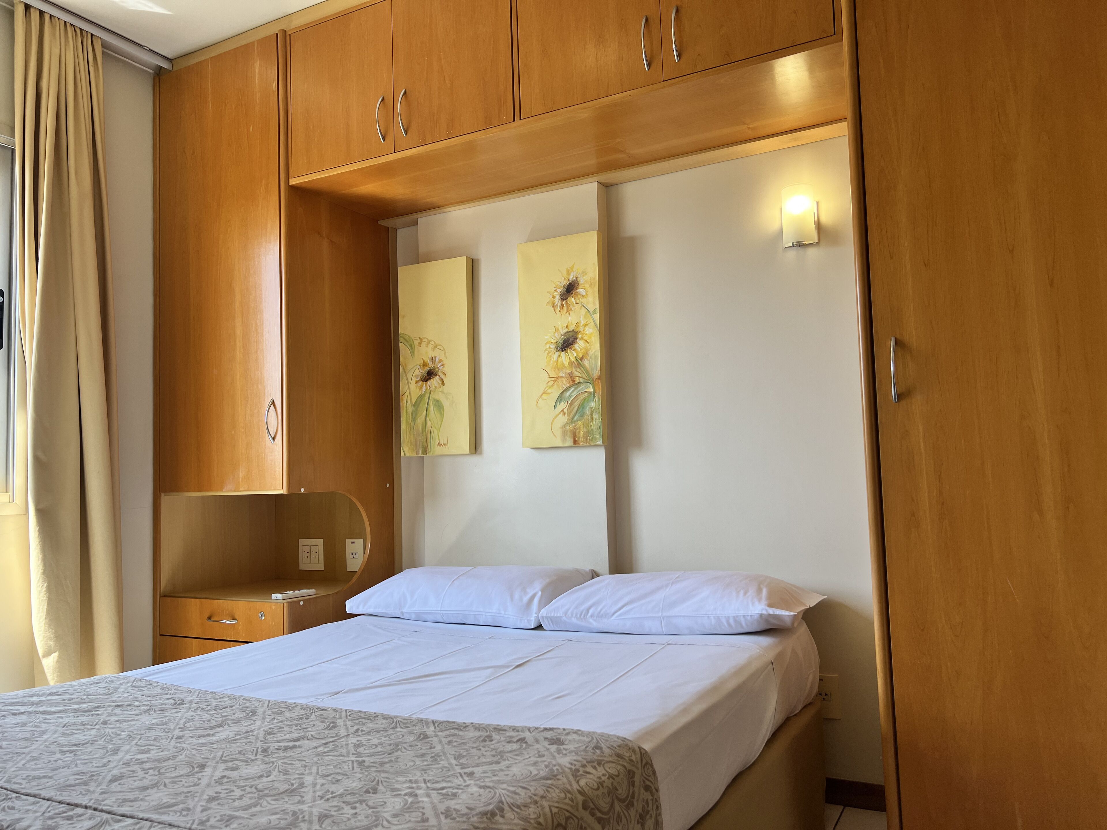 A bedroom with a bed, wooden wardrobe, a nightstand, and wall art.