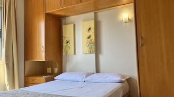 A bedroom with a bed, wooden wardrobe, a nightstand, and wall art.