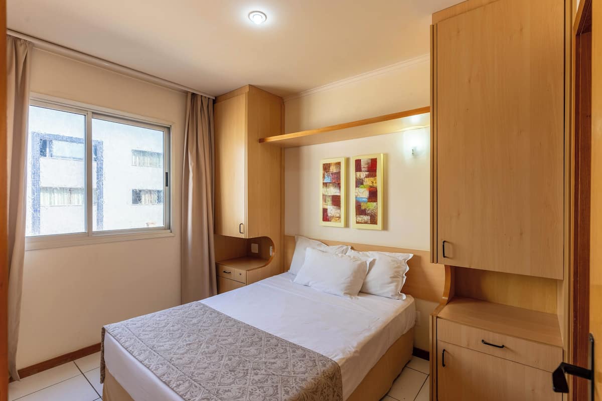 Une chambre à coucher comprenant un lit, une table de chevet, une armoire en bois et une fenêtre avec des rideaux.