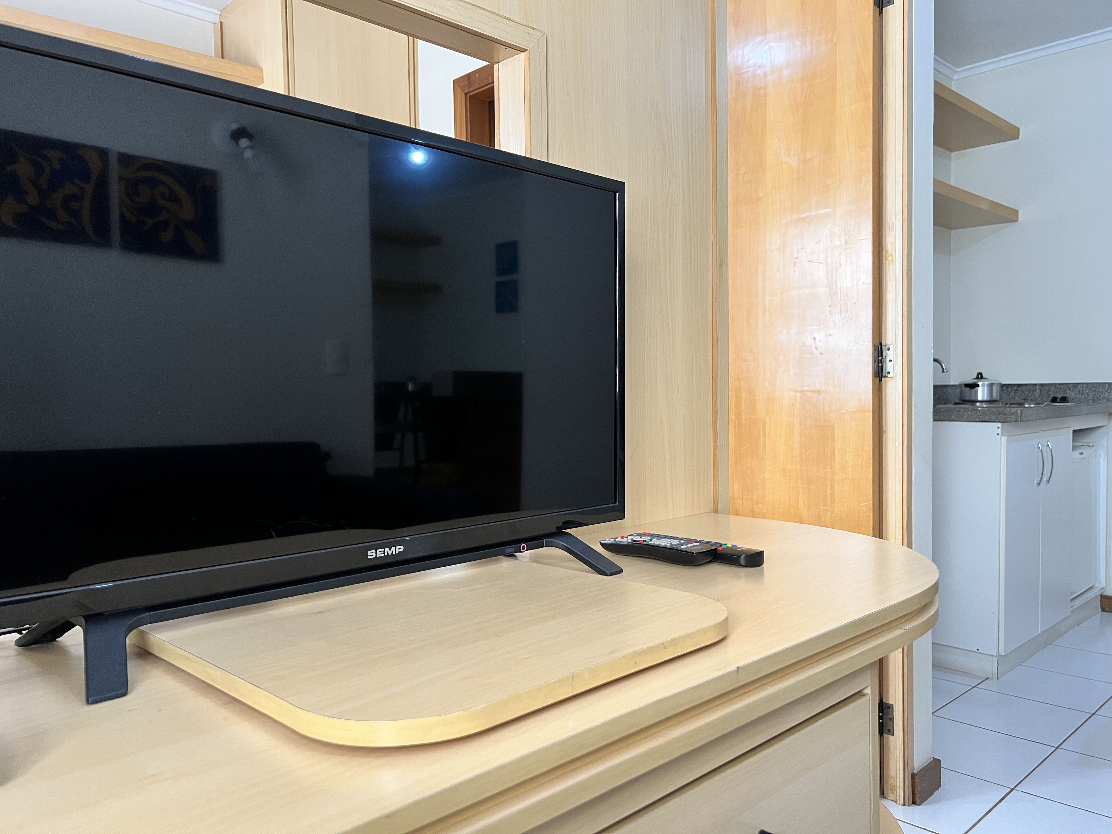 Un televisor de pantalla plana sobre un soporte de madera en una habitación con una cocina visible al fondo.