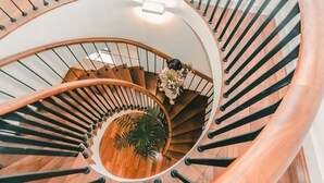 A spiral staircase with wooden steps and black railings, a potted plant, and a vase with flowers at the top. - Ficus Suites Apartment (Hanoi)