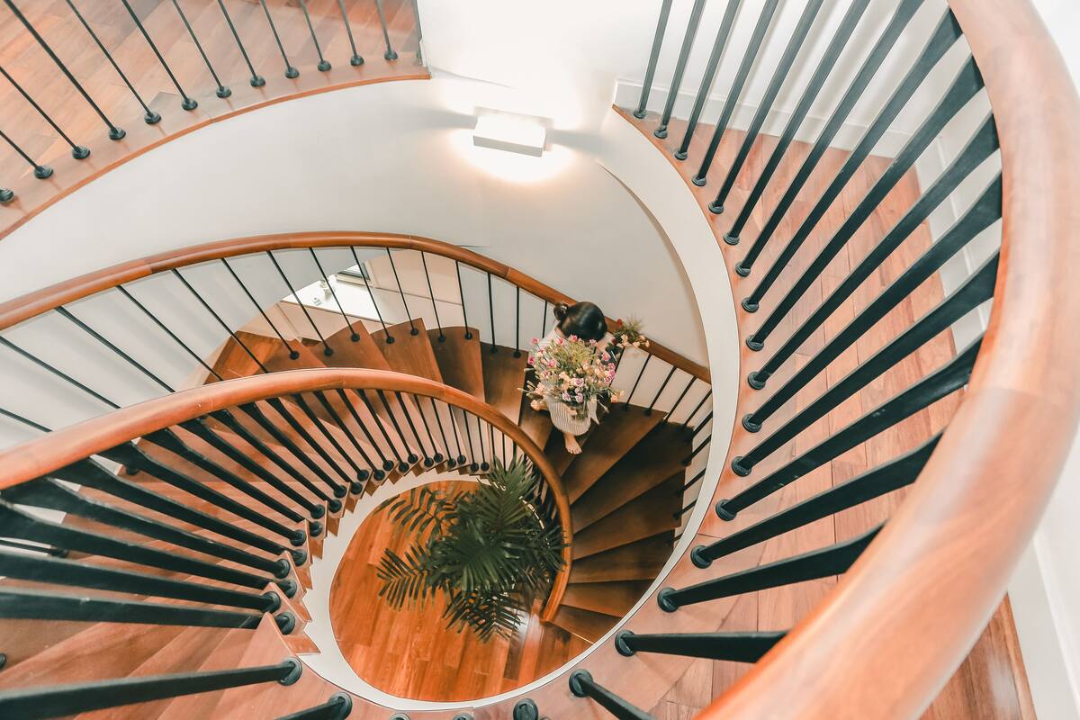 A spiral staircase with wooden steps and black railings, a potted plant, and a vase with flowers at the top.