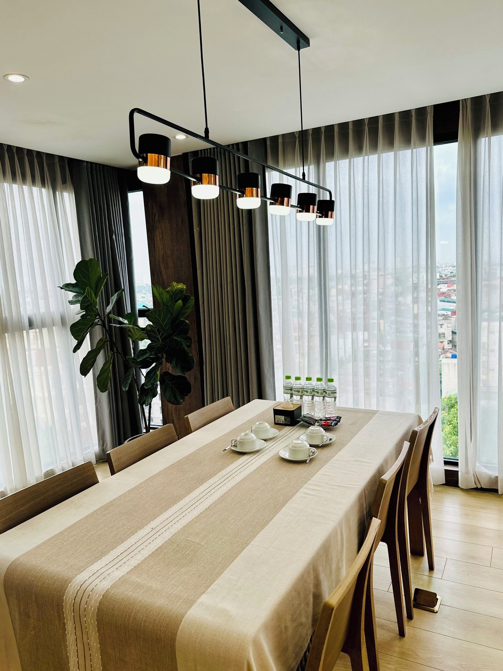 A modern dining area with a long table, chairs, and a city view through large windows.