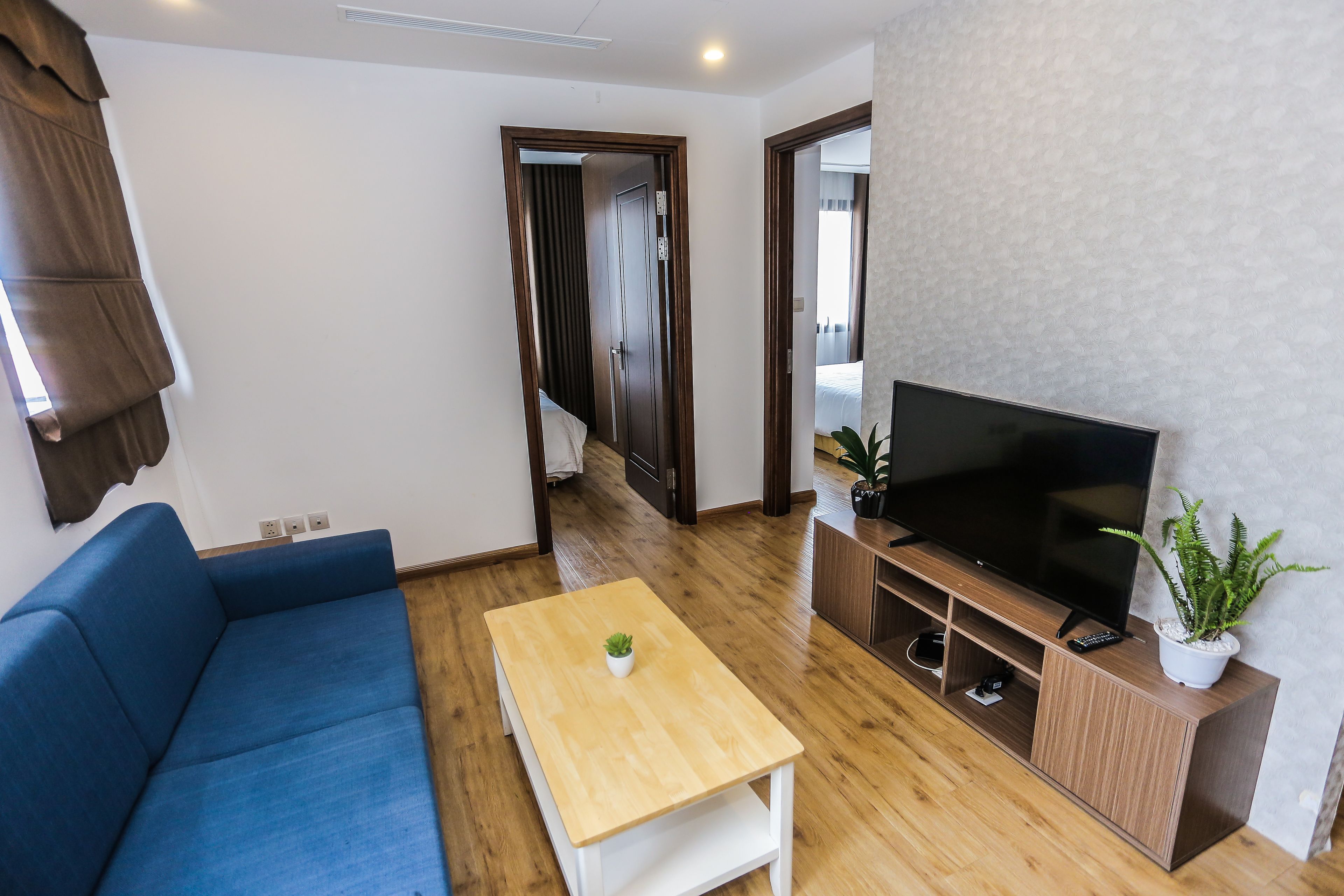 Una sala de estar moderna con un sofá azul, una mesa de centro de madera, un televisor sobre un mueble de madera y una planta en maceta.